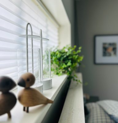 Två lovebirds, en Design house stockholm ljusstake och en krukväxt i ett fönster.