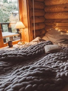Sovrum med en mysig säng, stickad filt och bordslampa i en trästuga.
