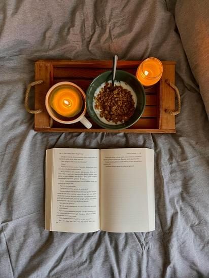 Frukostbricka med skål, kaffekopp och tända ljus, med en öppen bok nedanför.