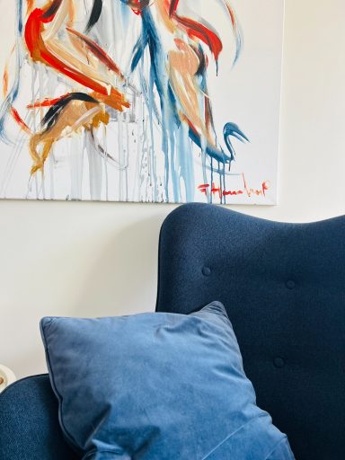 Blå fåtölj med en kudde och en färgglad målning på väggen bakom.