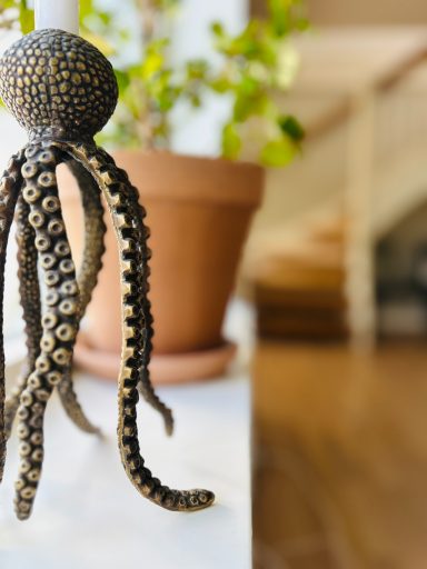 Dekoration av en bläckfisk i metall, stående nära en krukväxt.